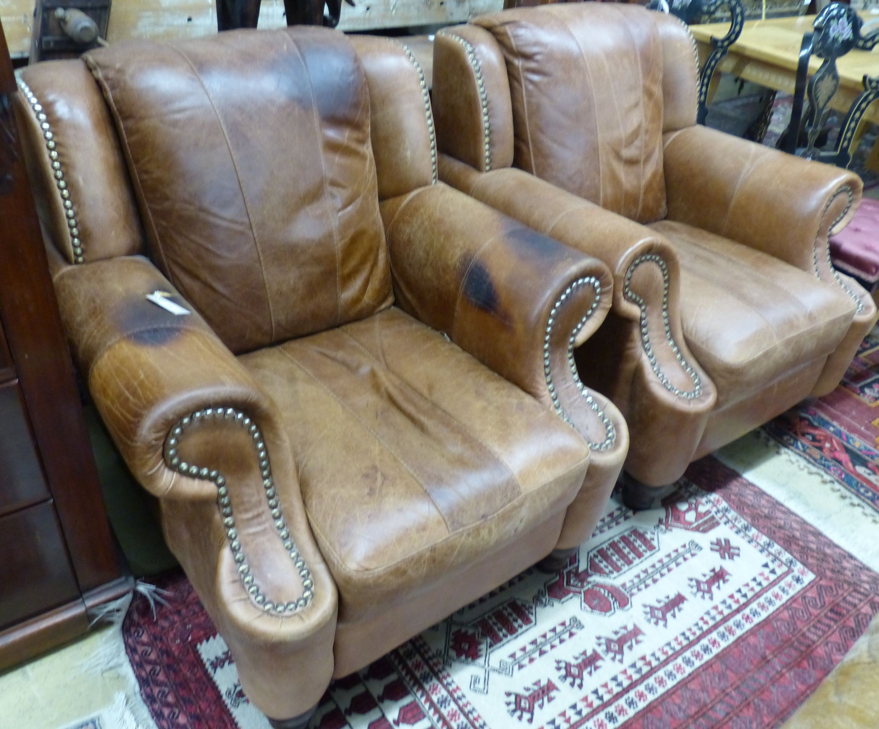 A pair of tan leather armchairs, W.94cm D.94cm H.90cm (one arm holed)